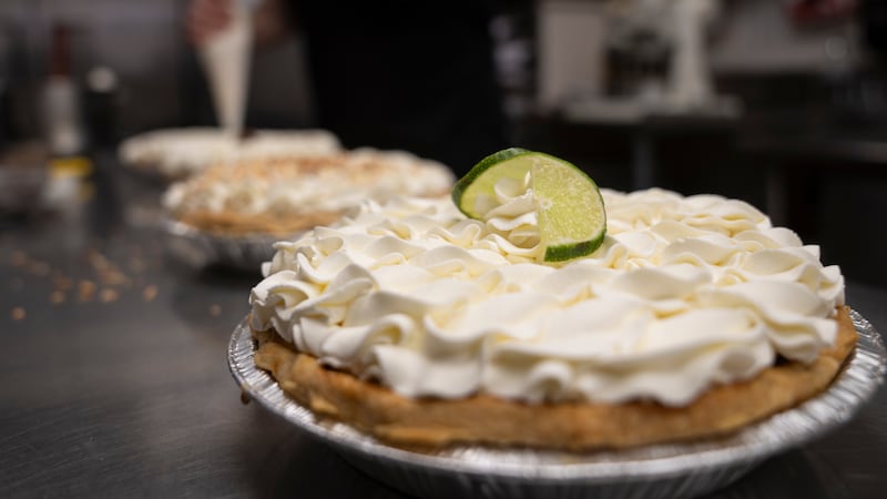 A freshly decorated Key Lime pie rests on a counter in a busy bakery kitchen at Michele's...